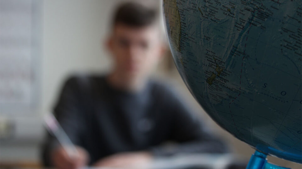 Photograph of a student studying Geography next to a globe