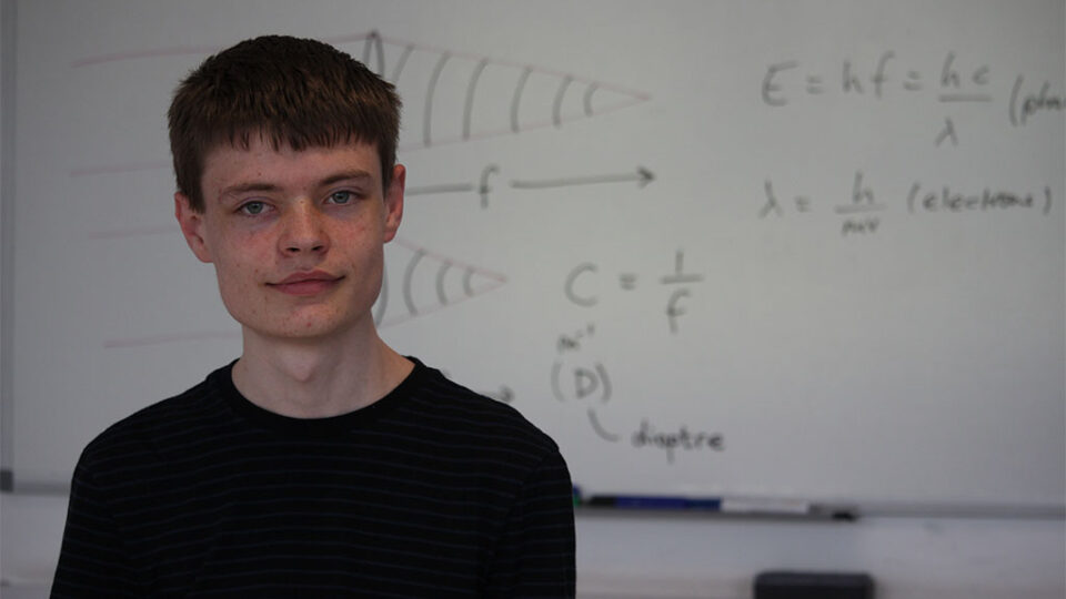 Photograph of a physics student stood in front of a whiteboard.