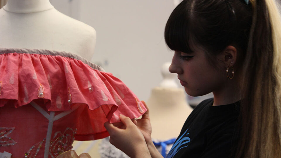 Photograph of a textiles student standing next to a dress she has made.